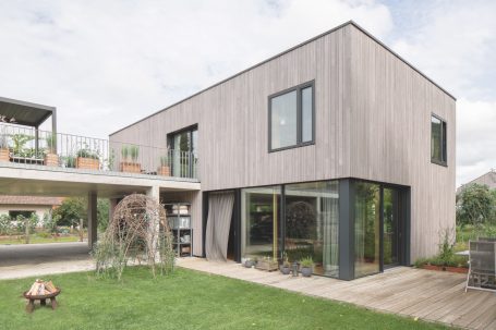 Modernes Holzhaus mit Flachdach, großen Fenstern und grünem Gartenbereich.